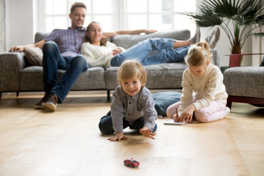 Cute,Kids,Playing,While,Parents,Relaxing,Sofa,At,Home,Together,